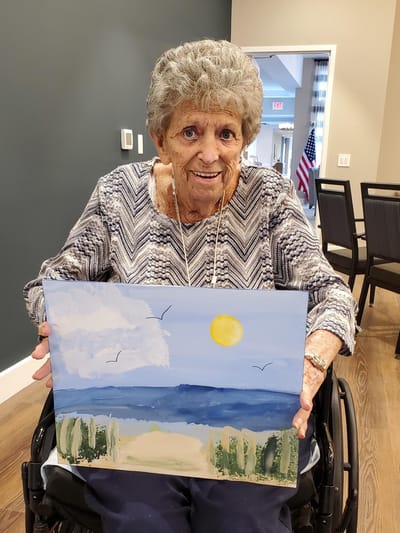 Elderly woman displaying her painting in a common area.