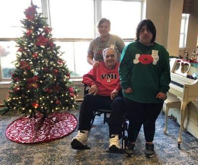 Residents and staff celebrate by a decorated Christmas tree.