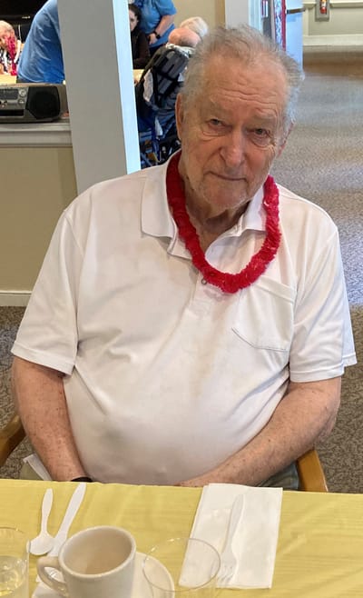 Elderly man wearing a lei in dining area.