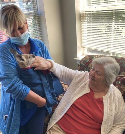 Resident interacting with staff and a small dog indoors.