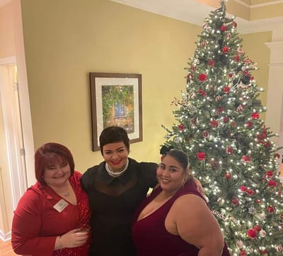 Three women celebrating in front of a decorated Christmas tree.