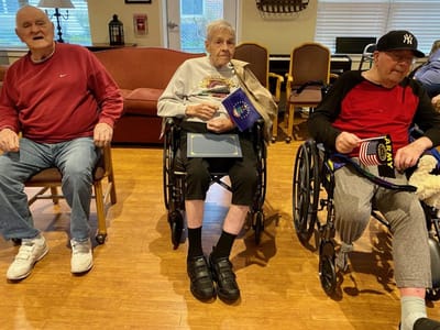 Three elderly residents in wheelchairs engaging in a group setting.