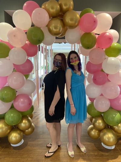 Two women posing in front of a colorful balloon arch.