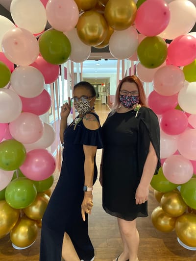 Two women posing in festive attire among balloons