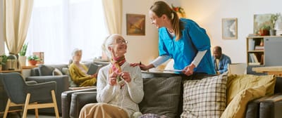 A caregiver interacts with a smiling resident in a cozy common area.