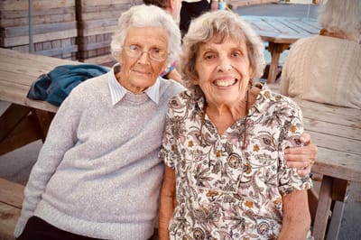 Two elderly women smiling together at a picnic table