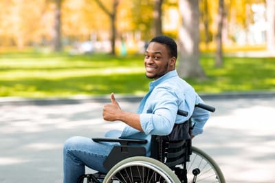 A smiling man in a wheelchair giving a thumbs up outdoors