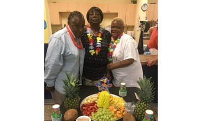 Residents enjoying a festive fruit display with leis