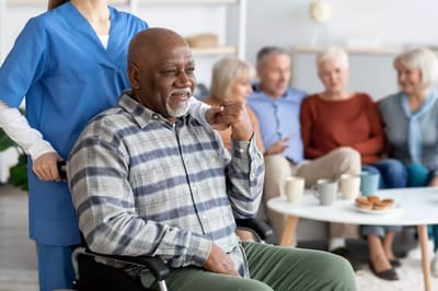 A resident in a wheelchair with staff and other residents in the background