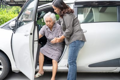 Caregiver assisting an elderly woman exiting a vehicle