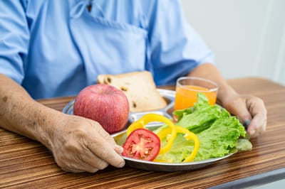 A resident holding a healthy meal with vegetables and fruit