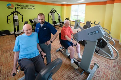 Residents exercising with staff assistance in a fitness area