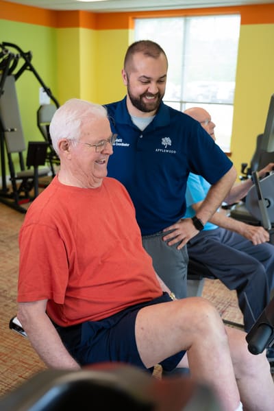 Resident exercising with staff assistance in a gym room