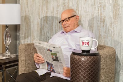 An older man reading a newspaper in a cozy corner