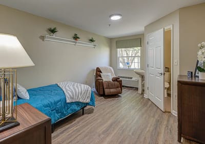 A cozy private resident room with a chair and bed