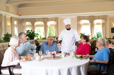 Residents enjoying a meal with a chef in a dining room