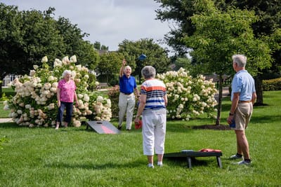 Residents playing cornhole in a lush garden area