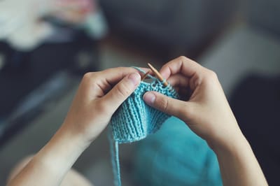 Hands knitting a blue scarf with yarn