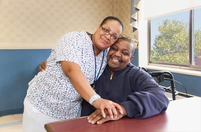 A caregiver and resident smiling in a facility's interior