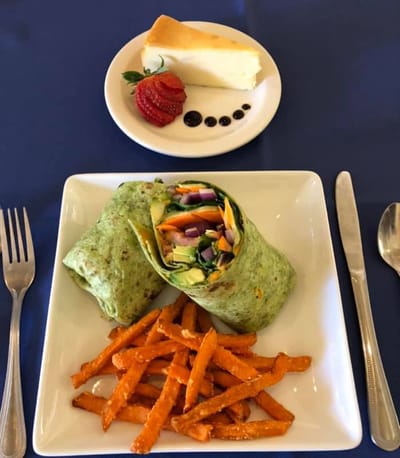 A plate with a spinach wrap, sweet potato fries, and cheesecake