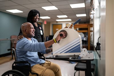 Resident engaging in therapy exercise with staff assistance