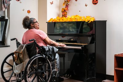 A resident in a wheelchair playing the piano indoors