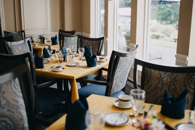 A dining room set up for a meal with tables and place settings