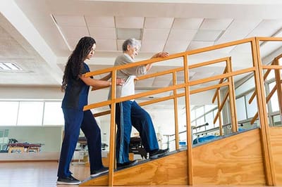 Staff assisting a resident on a staircase in a therapy room.