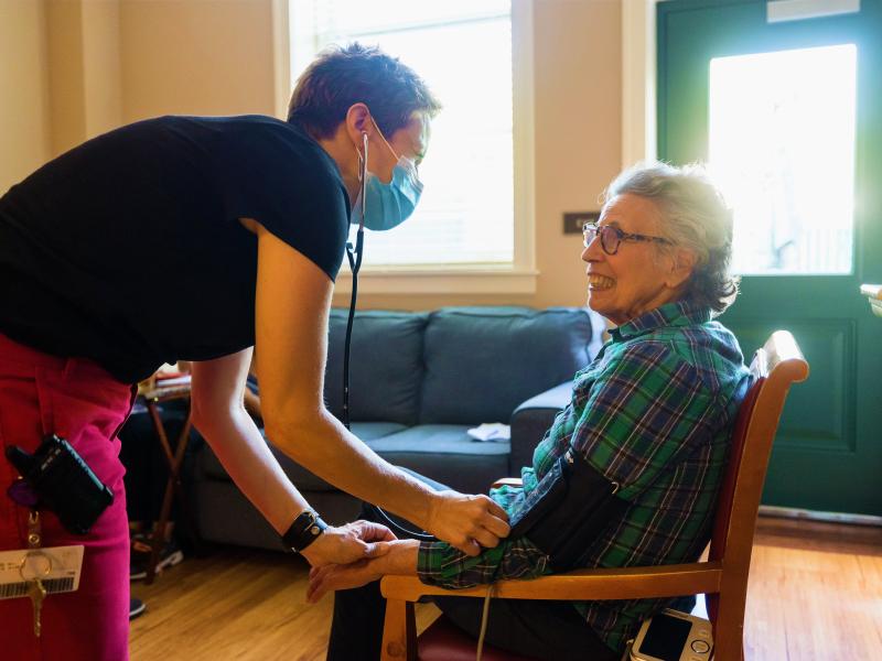 Nurse taking blood pressure of a smiling resident in a cozy room