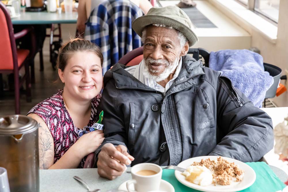 A resident and staff member smiling in the dining area