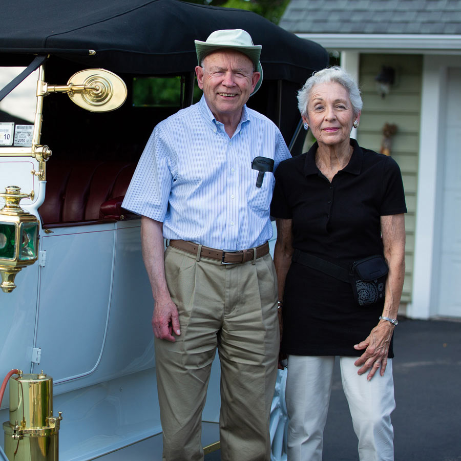A senior couple posing by a classic car