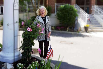 A resident smiling by flowers outside the facility