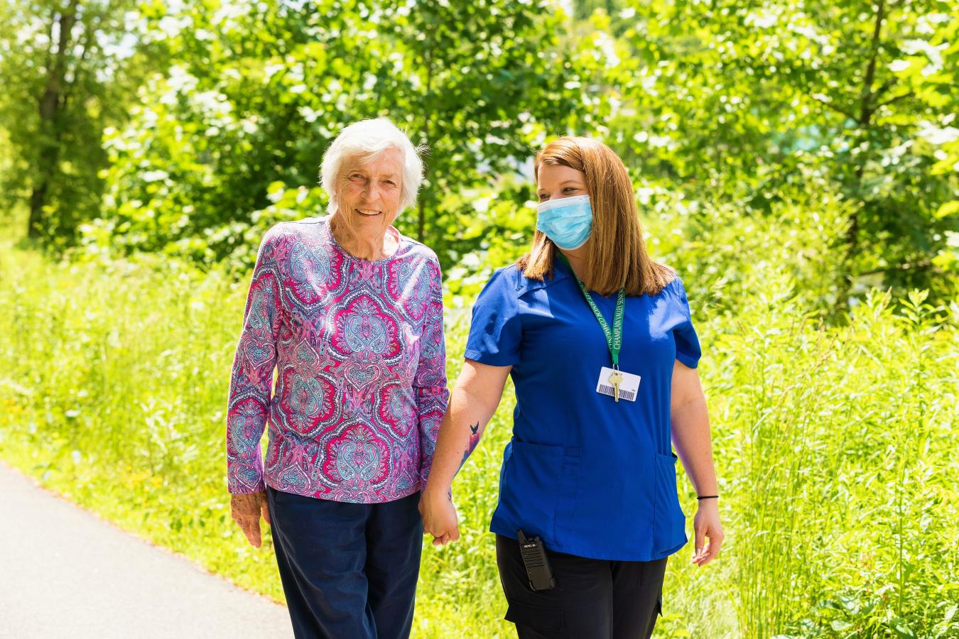 A resident walking with a caregiver in a lush outdoor area