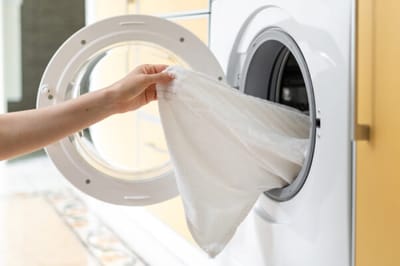 A hand placing linens into a washing machine