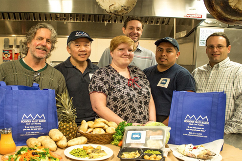 Staff members with prepared meals in the kitchen