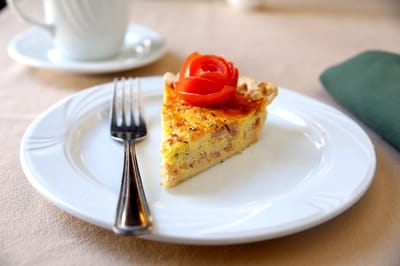 A slice of quiche garnished with a tomato rose