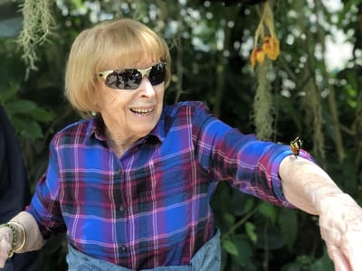 Senior woman smiling outdoors with a butterfly on her arm