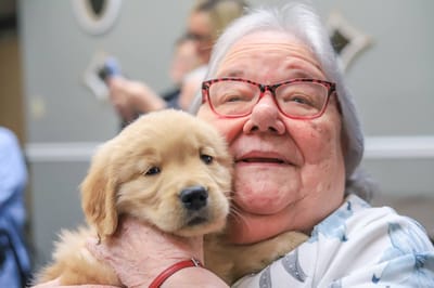 Resident smiling with a puppy in a common area