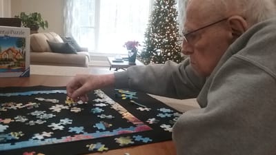 An elderly man working on a jigsaw puzzle indoors
