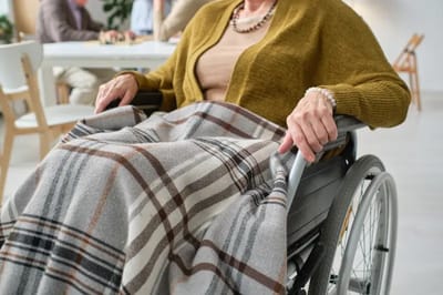 Resident in a wheelchair with a plaid blanket in a common area