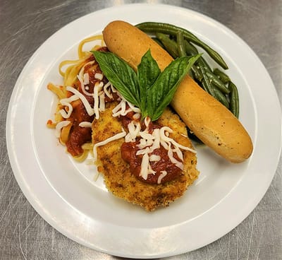 A plate of chicken parmesan with sides of pasta and green beans