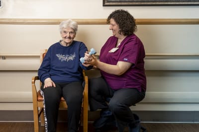 A staff member assisting a resident with weights in a care facility