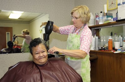 Stylist using a hairdryer on a resident's hair in a salon.