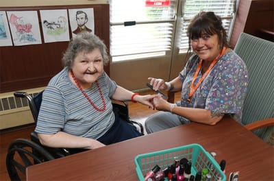 Staff member painting resident's nails in a cozy interior