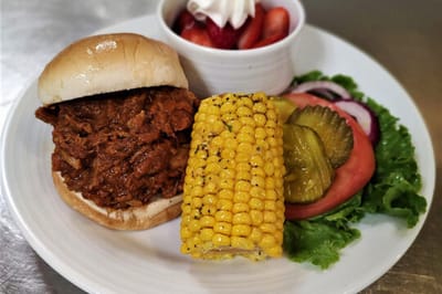 A delicious meal served at the facility, featuring pulled pork sandwich and corn
