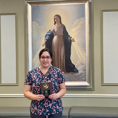 Staff member holding an award in front of a painting
