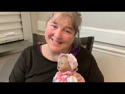 Resident smiling with a doll in an interior setting