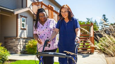 Staff assisting a resident outdoors with a walker