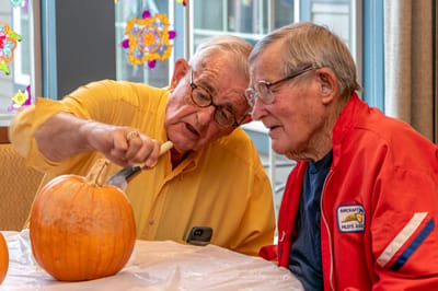 Two residents carving a pumpkin together at a table
