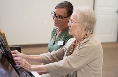 A staff member assisting a resident at a piano